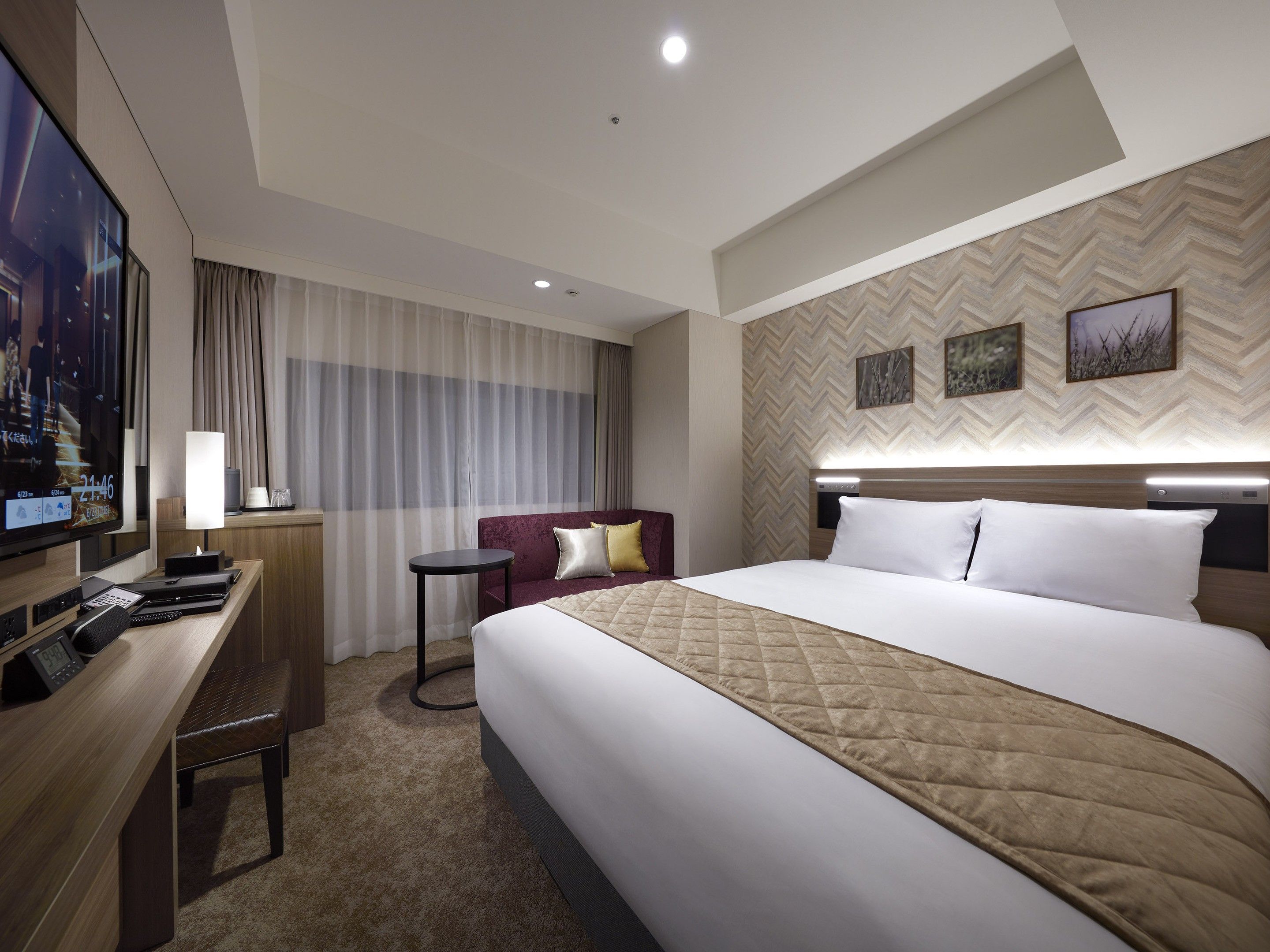 A hotel room with a bed, a desk, a TV, and a view of the city.