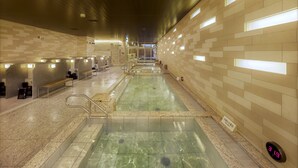 Una piscina interior moderna con suelo y paredes de azulejos, bancos y una pantalla digital que muestra la temperatura.