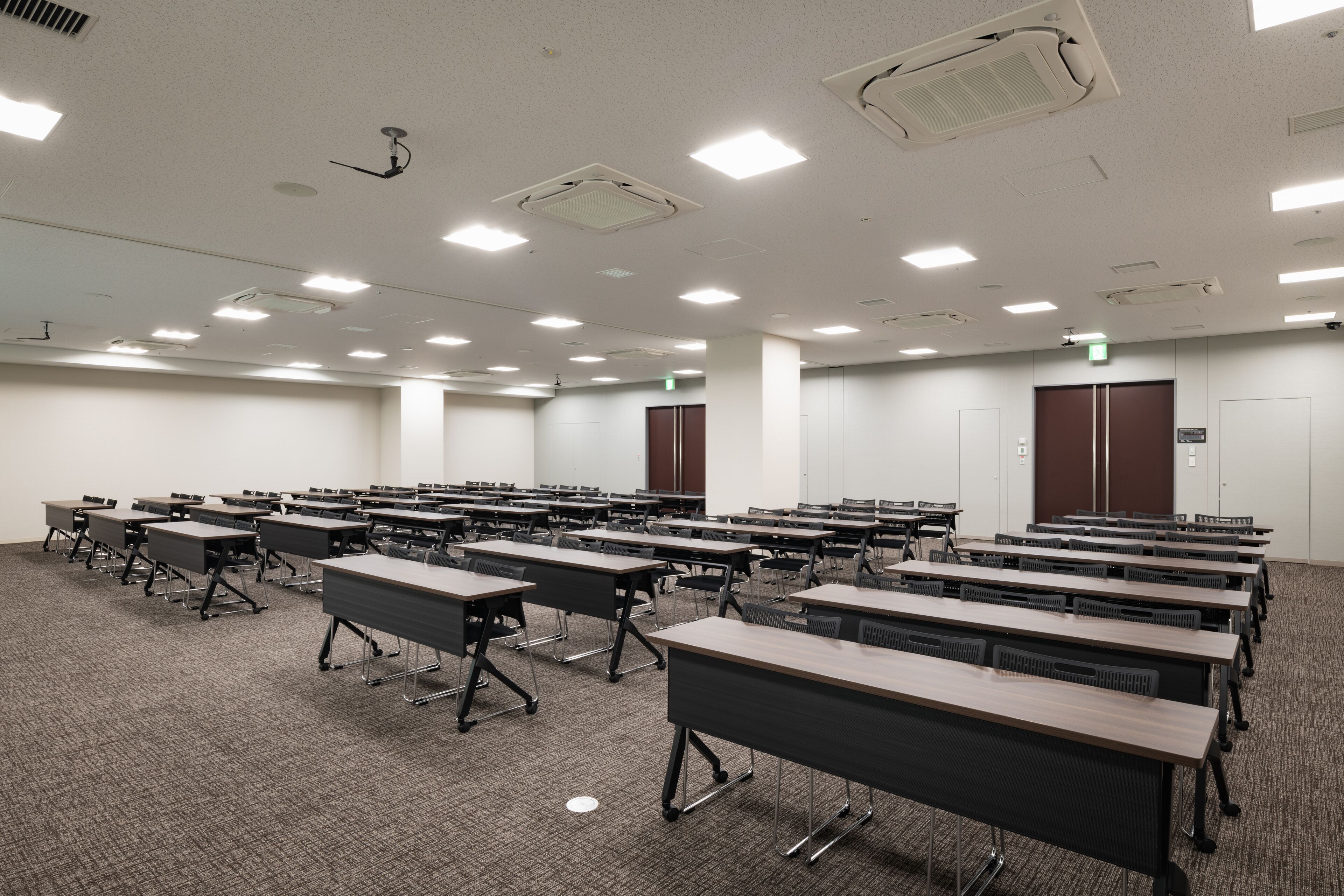 Une salle de conférence dotée de plusieurs tables et chaises, de murs blancs et d’un éclairage au plafond.