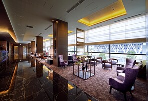 Eine geräumige Lobby mit Marmorboden, einer Sitzecke mit violetten Stühlen, einem Empfangsbereich und großen Fenstern mit Blick nach außen.