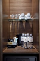 Eine Minibar mit einem Glasregal, das Tassen und eine Auswahl an Kaffee- und Teebeuteln beherbergt.