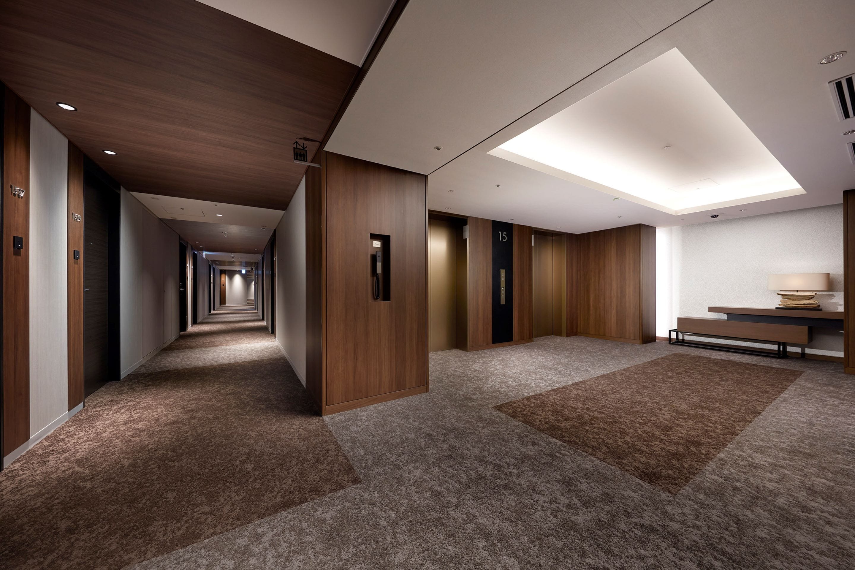 A modern hotel corridor with wooden paneling, carpeted floors, and a skylight.