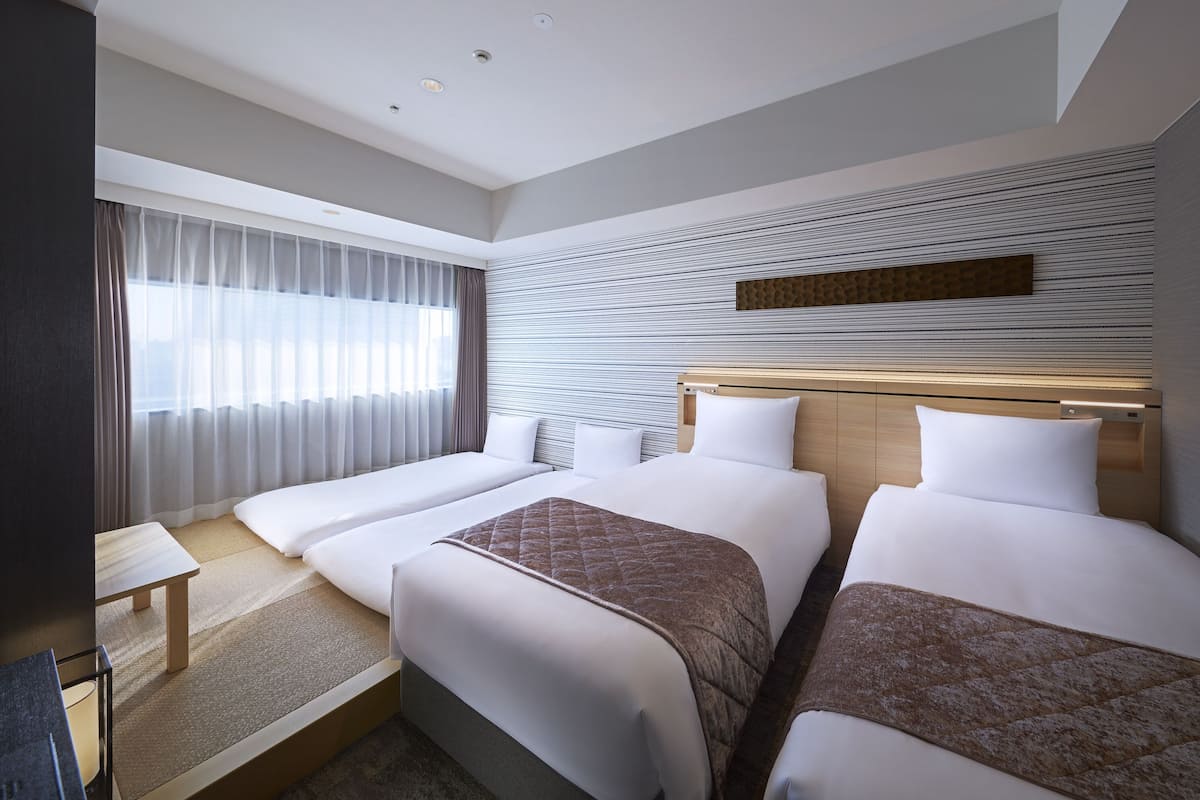 Une chambre d’hôtel avec deux lits, un bureau et une grande fenêtre avec des rideaux.