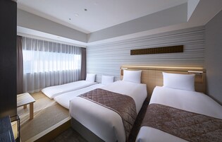 A hotel room with two beds, a desk, and a large window with curtains.