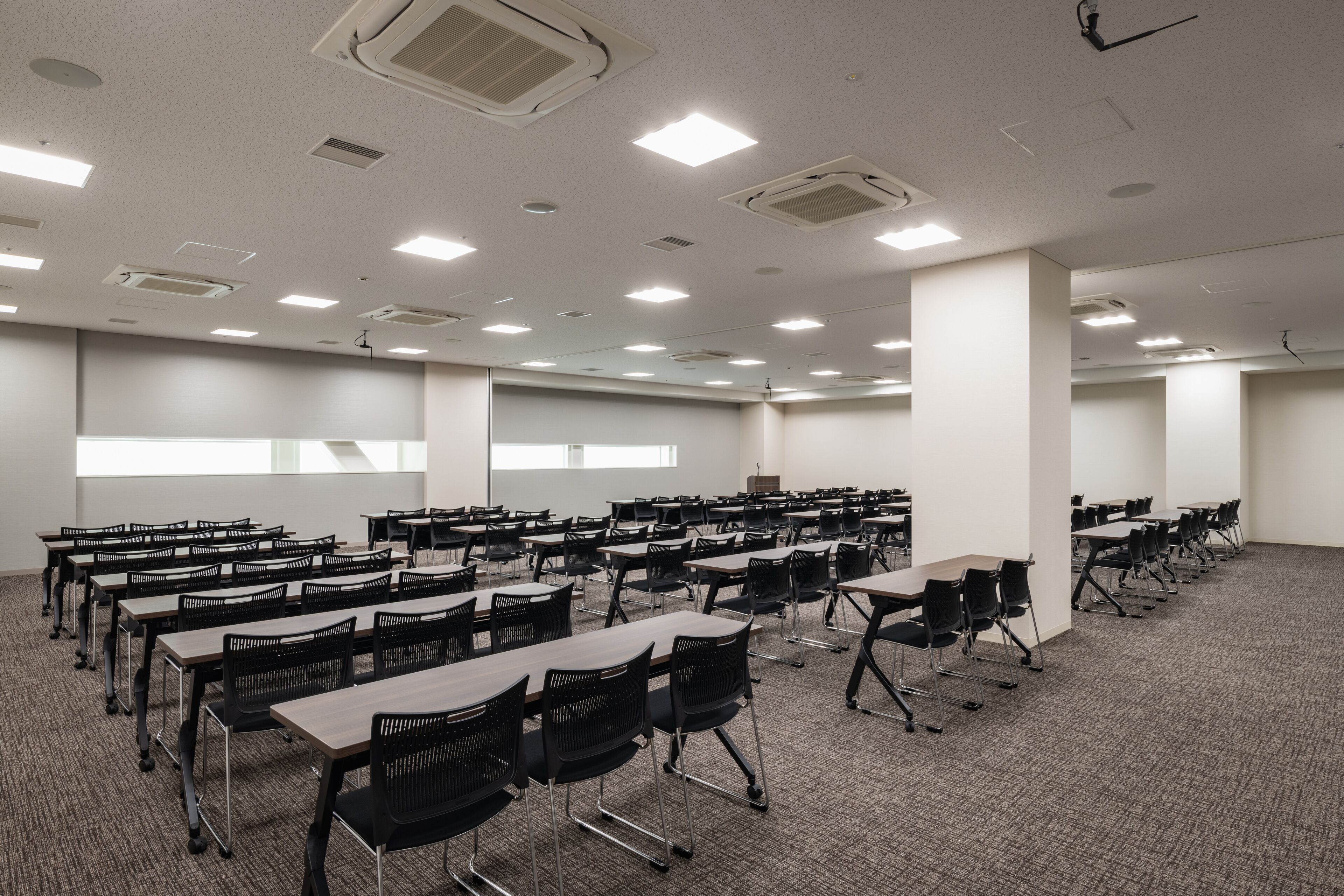 Un salón de conferencias con varias mesas y sillas, paredes blancas y luces en el techo.