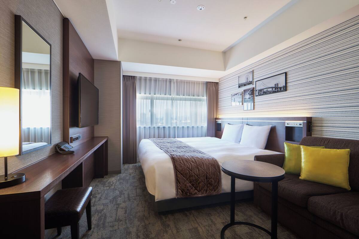 Une chambre d’hôtel équipée d’un lit, d’un bureau, d’une chaise, d’une petite table, d’un canapé et d’une télévision.