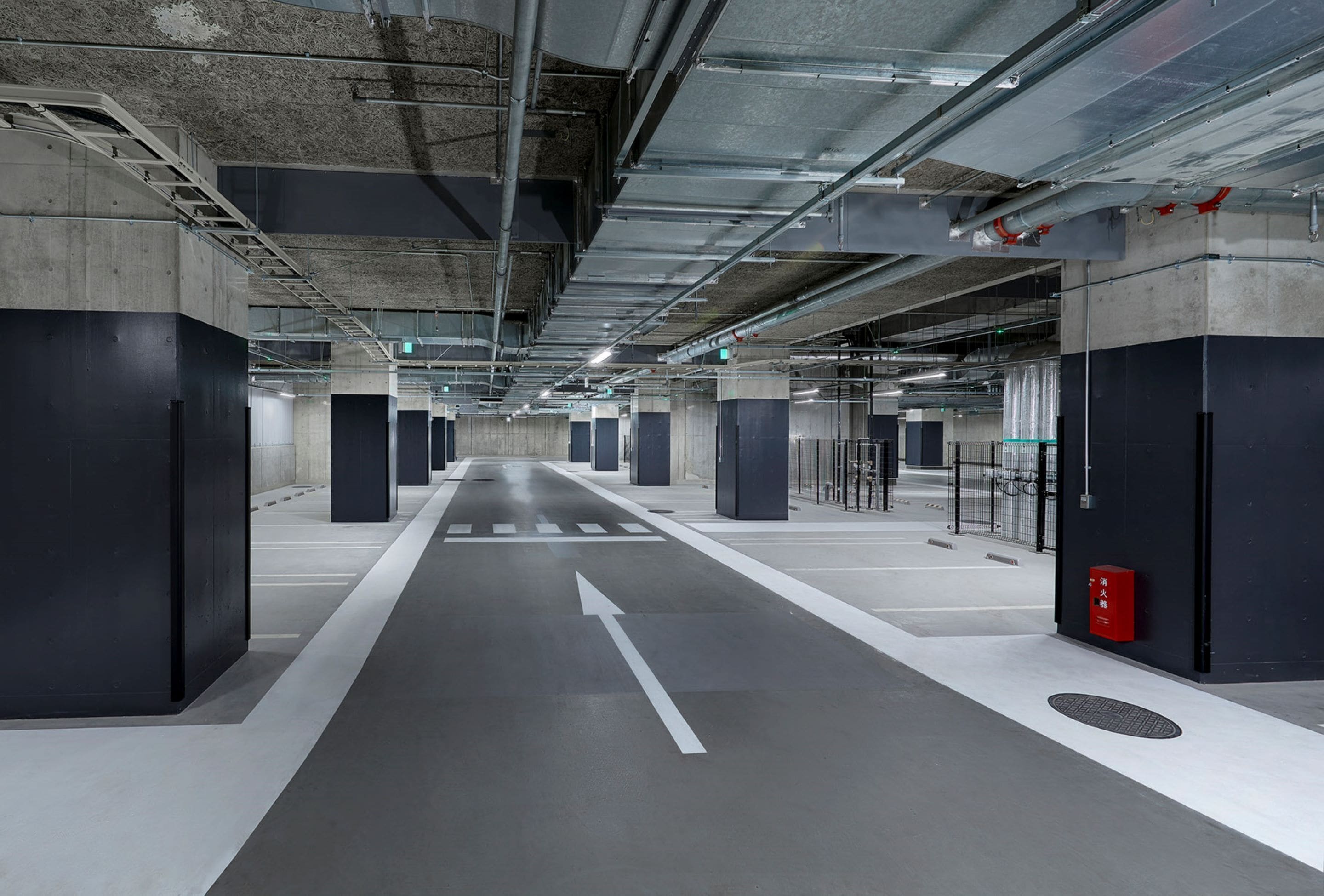 A modern underground parking garage with concrete pillars, directional arrows on the floor, and a fire extinguisher on the right.