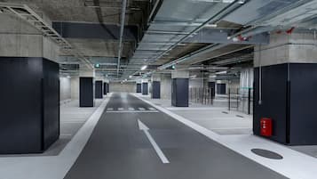 A modern underground parking garage with concrete pillars, directional arrows on the floor, and a fire extinguisher on the right.