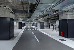 Eine moderne Tiefgarage mit Betonsäulen, Pfeilen zur Orientierung auf dem Boden und einem Feuerlöscher rechts.