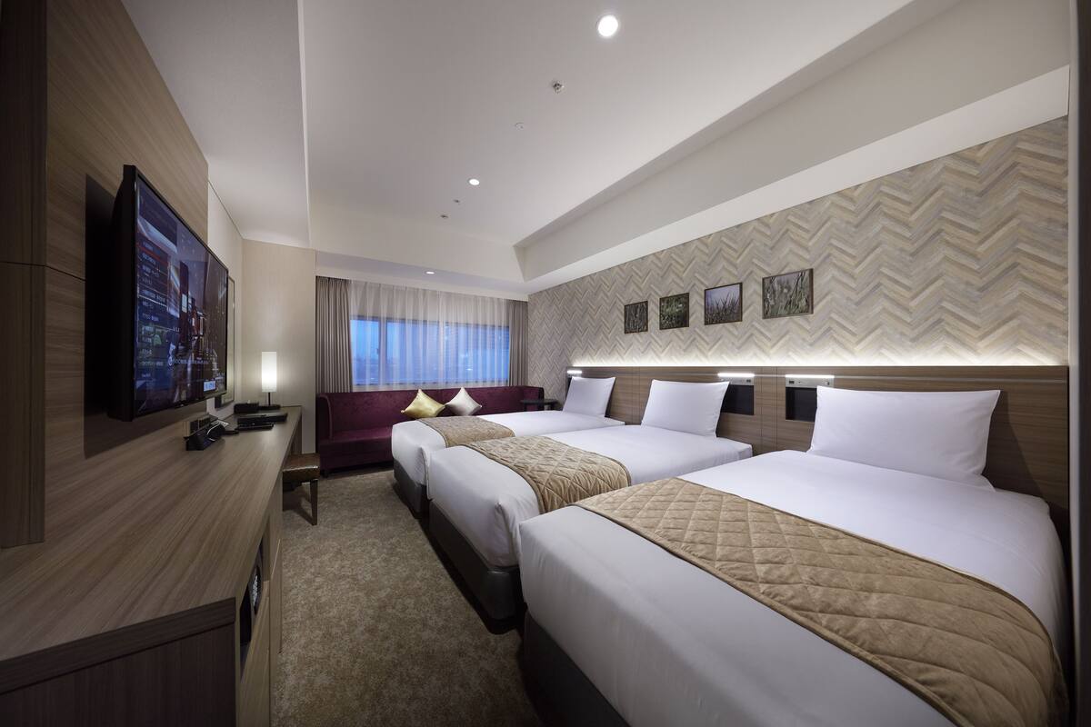 Une chambre d’hôtel avec deux lits, une télévision, un bureau et une fenêtre avec des rideaux.