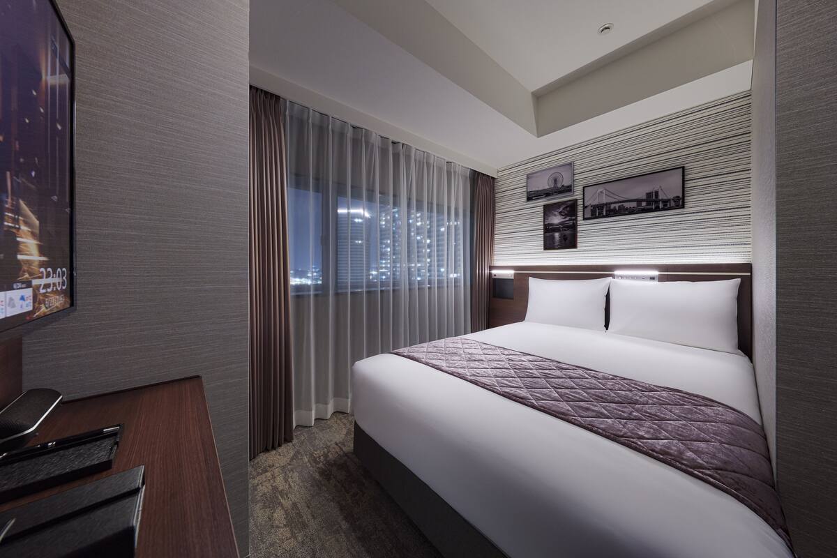 Une chambre d’hôtel moderne dotée d’un grand lit, d’un téléviseur à écran plat et offrant une vue sur la ville par la fenêtre.