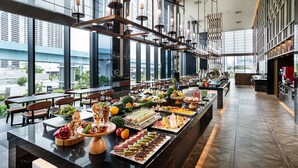 Un comedor amplio con una barra larga repleta de diferentes alimentos y vistas de la ciudad a través de amplias ventanas.