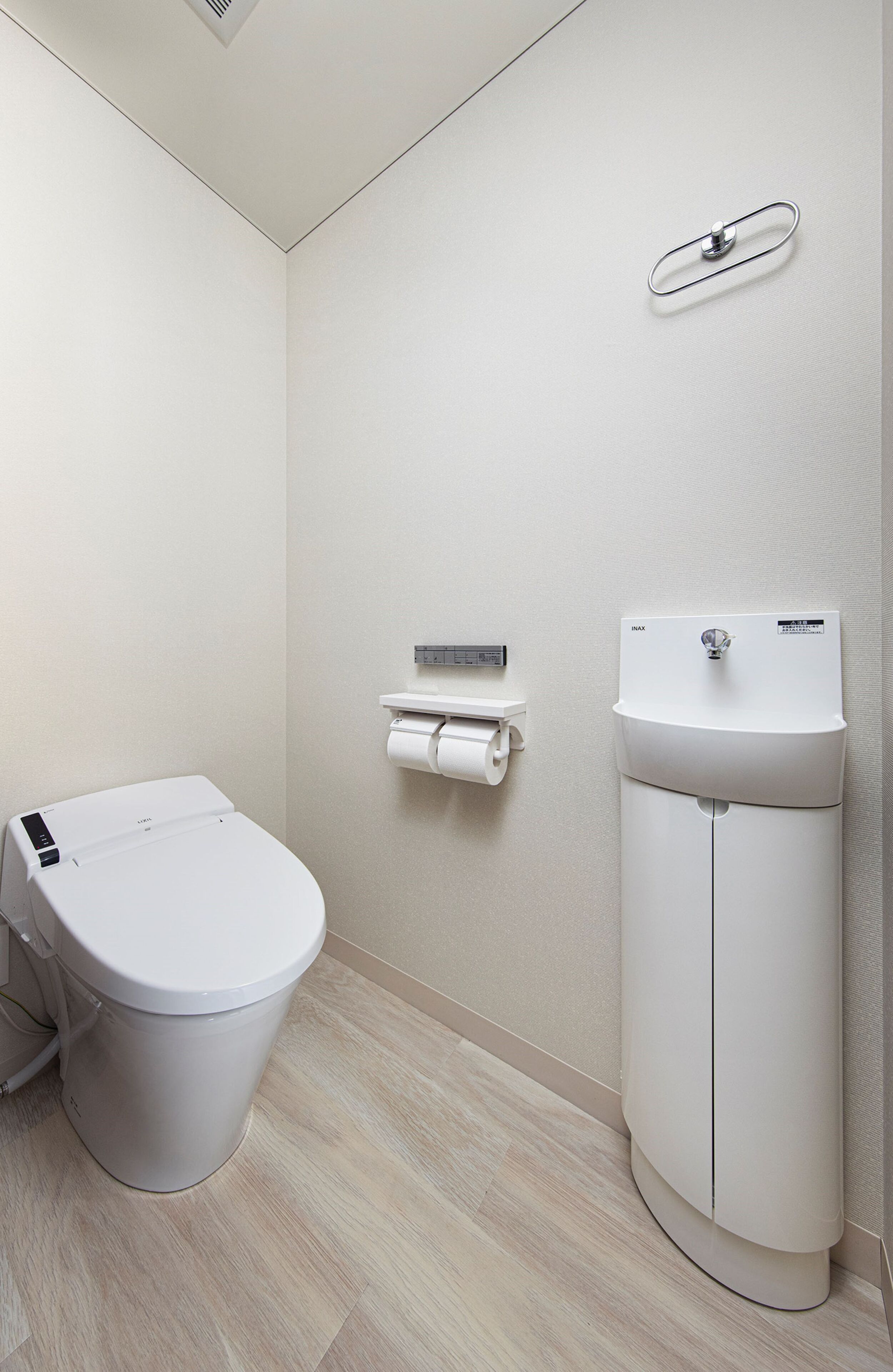 Un baño moderno con inodoro, dispensador de toallas de papel y lavamanos.
