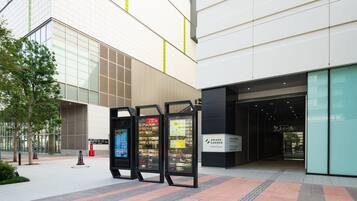 Una entrada moderna a un edificio con fachada de vidrio, un quiosco informativo digital y un cartel que indica Ariake Garden.