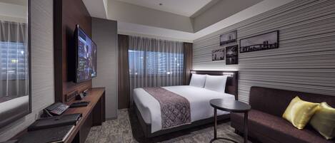 A modern hotel room with a large bed, a sofa, a desk with a computer, and a TV.