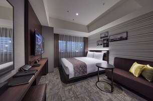 A modern hotel room with a large bed, a sofa, a desk with a computer, and a TV.