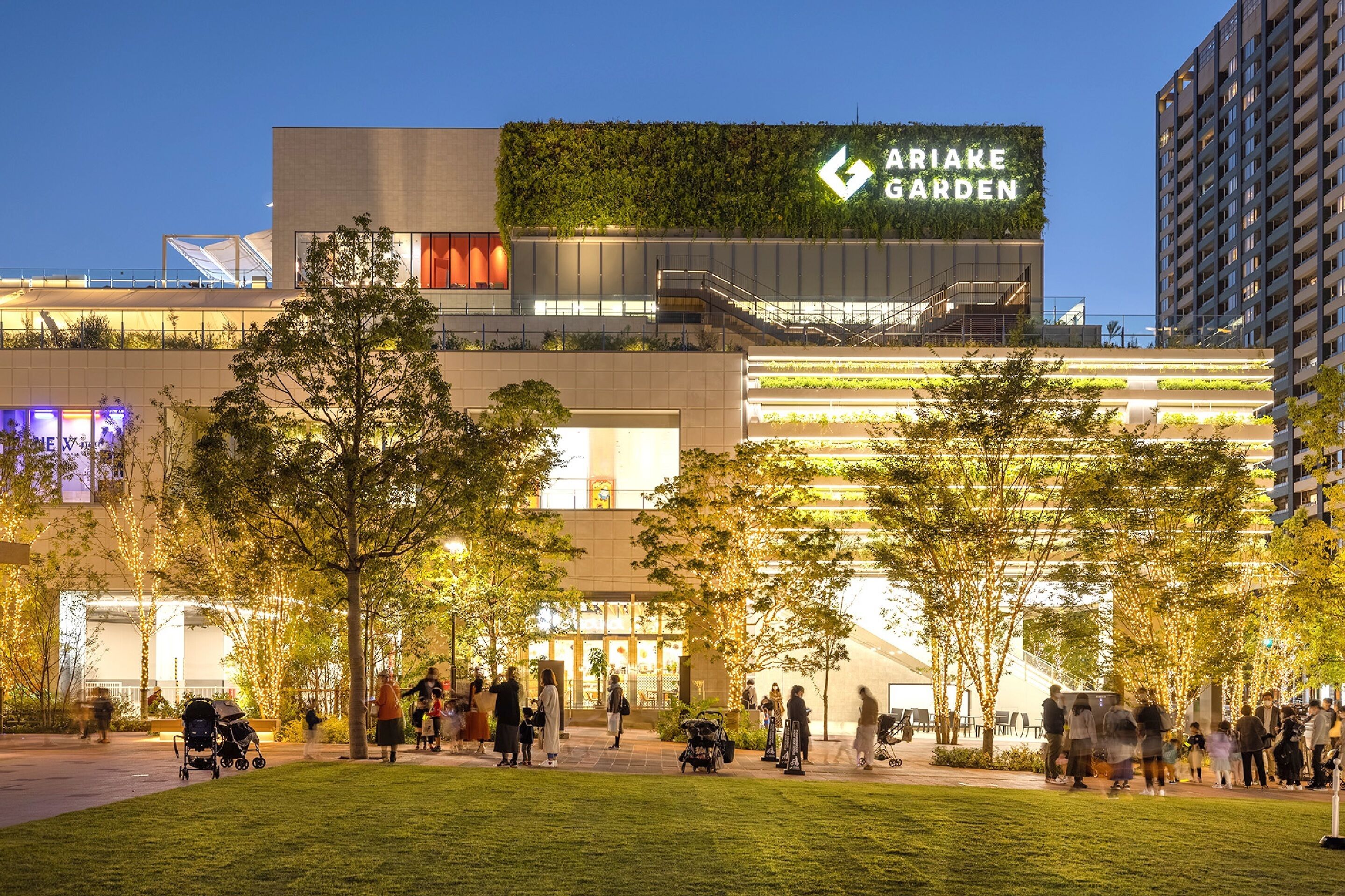 A modern building with a sign reading "Ariake Garden" and a well-maintained outdoor area with trees and people.