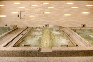 A large indoor hot spring bath with multiple entry points, tiled walls, and built-in lighting.