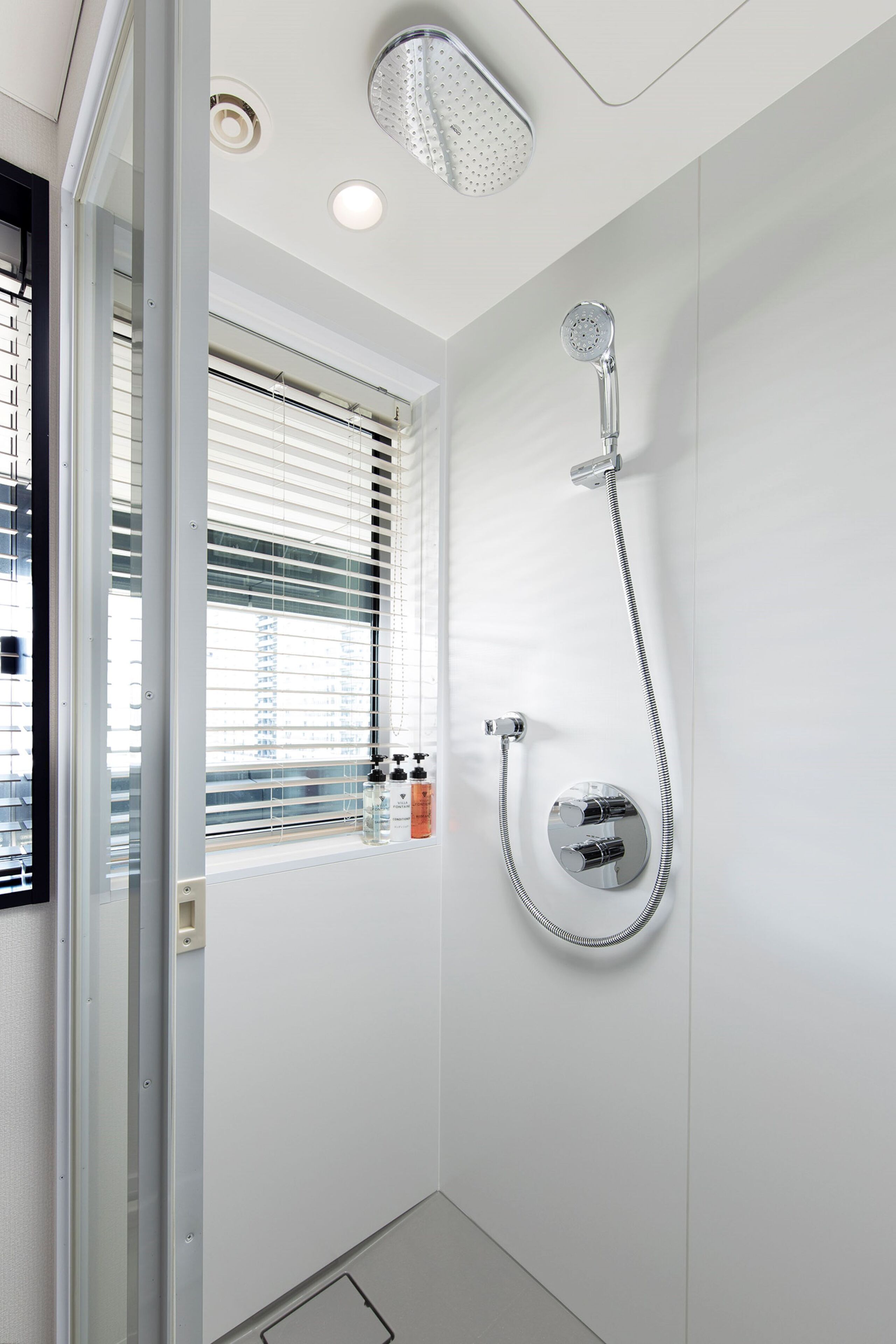 Un baño moderno con ducha, una ventana con persianas y un estante con artículos de aseo.