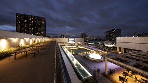 Terraza en la azotea con mobiliario, piscina y vistas nocturnas de la ciudad.