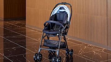 Ein Kinderwagen mit schwarzem Gestell und hellem Sitz, auf einem polierten Marmorboden in einer Halle mit Holzvertäfelung.