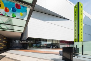 A modern building with a glass facade, a sign for 'ARIAGARDEN HOTEL', and a 'HOTEL THEATER' sign.