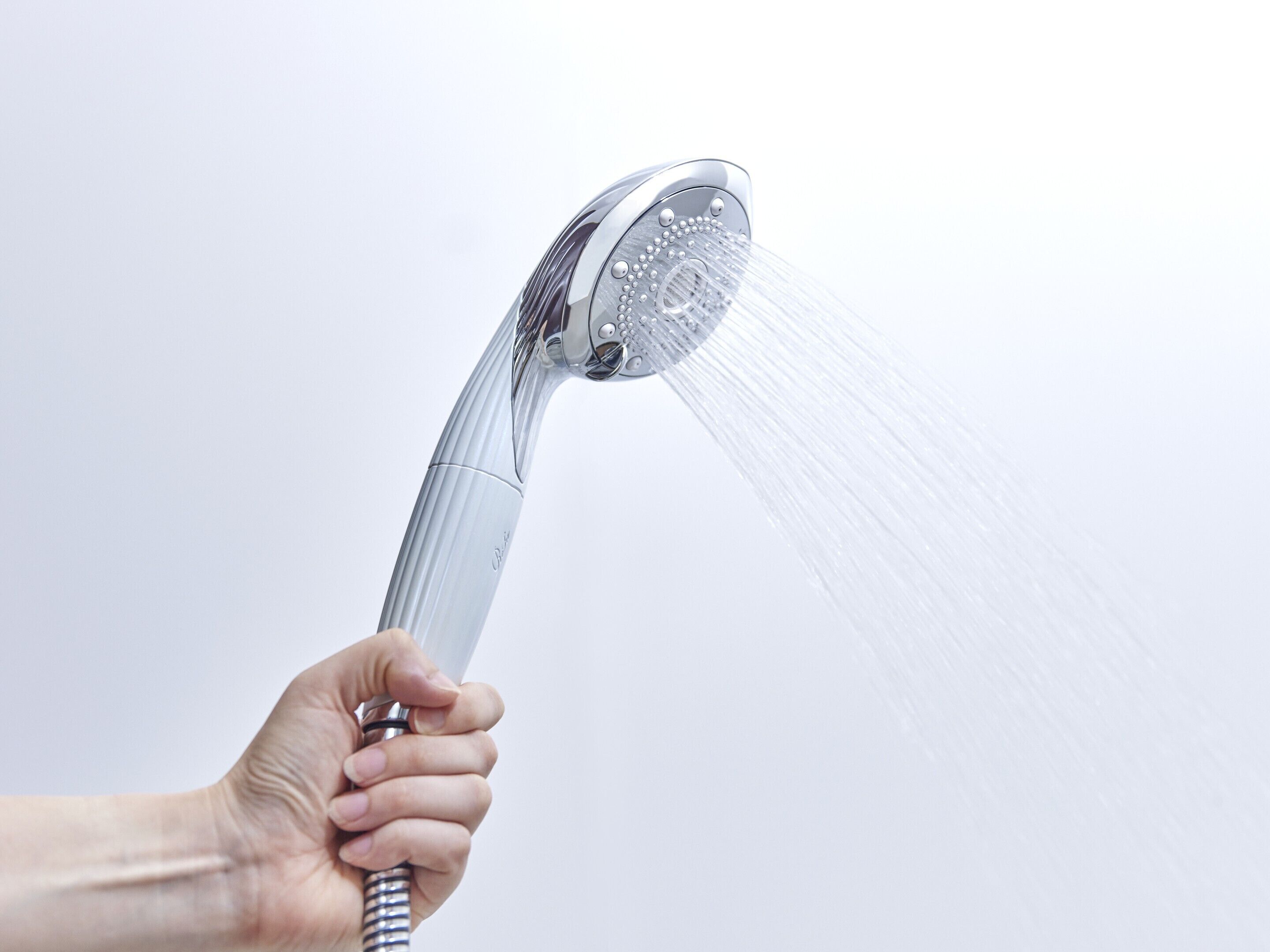 Una mano sosteniendo un cabezal de ducha con agua fluyendo.