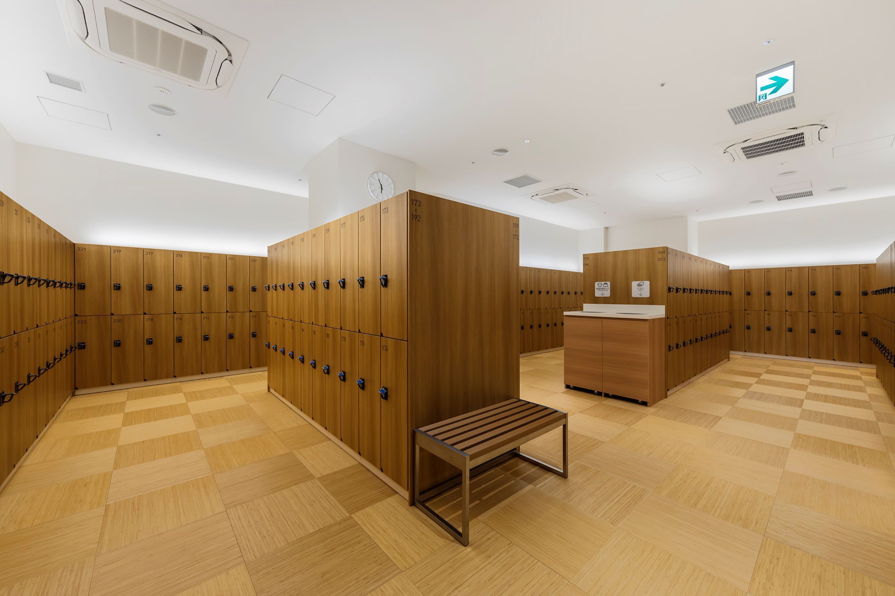 A modern locker room with wooden lockers, a bench, and a sink area.