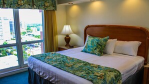 A hotel room with a large bed, a nightstand with a lamp, and a view of the city through a large window.