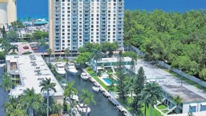 A high-rise hotel with multiple balconies, a marina with boats, and a view of the ocean.