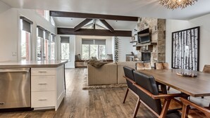 Una cocina moderna con lavavajillas incorporado, una zona de comedor con mesa y sillas de madera, y una chimenea de piedra.