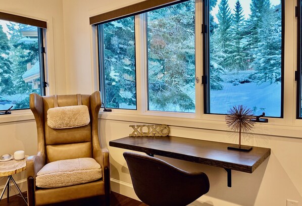 A room with a leather chair, a desk, and a view of snow-covered trees through large windows.