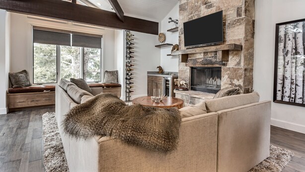 Una sala de estar moderna con chimenea de piedra, un sofá grande y un televisor montado.