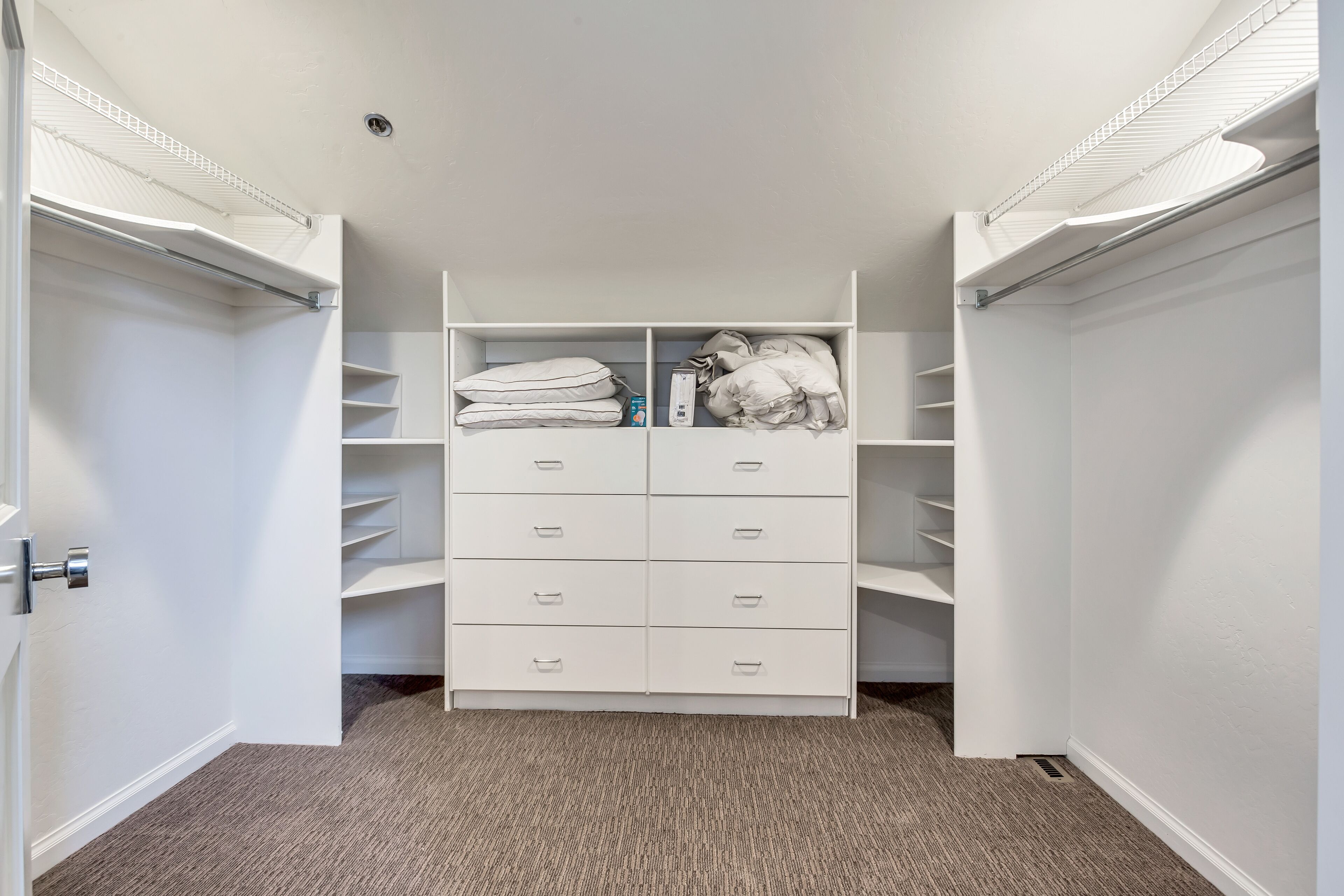 A walk-in closet with white shelving and drawers, a carpeted floor, and a white door.