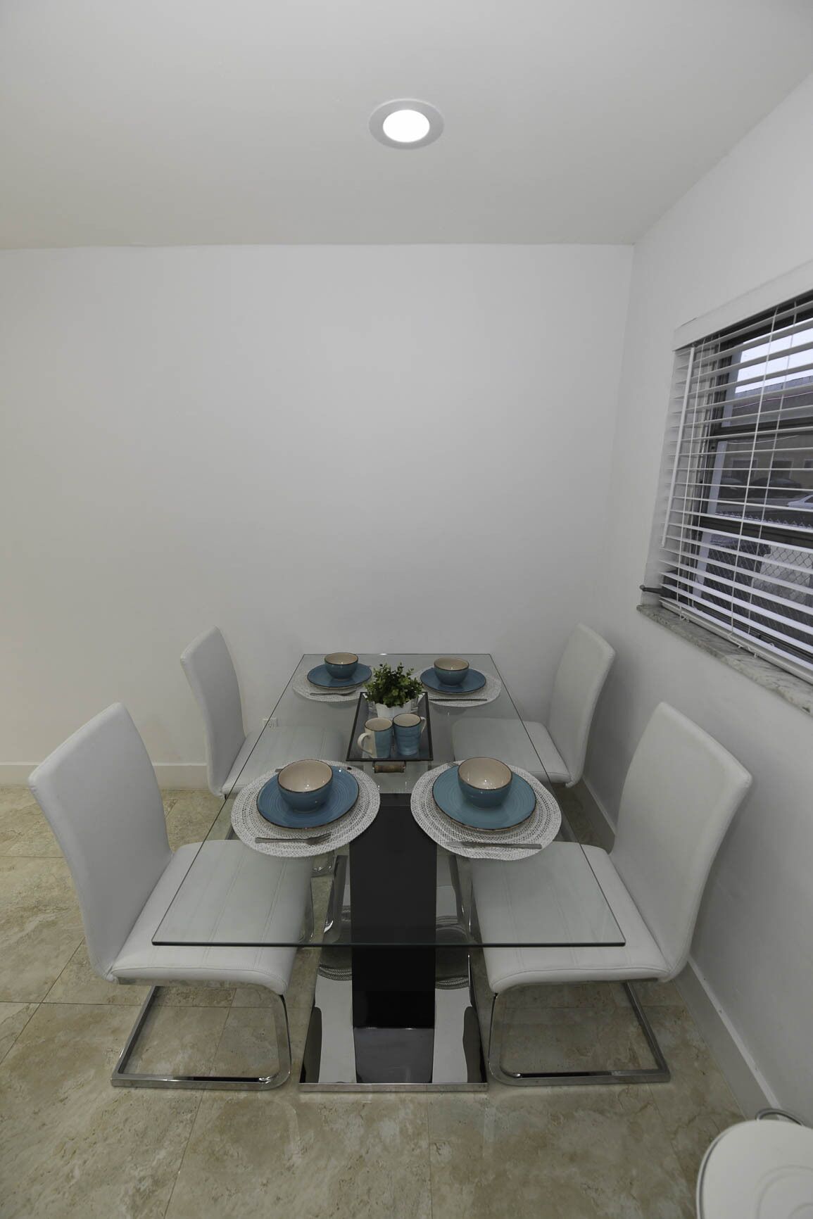 A dining area with a glass table, white chairs, and blue tableware.