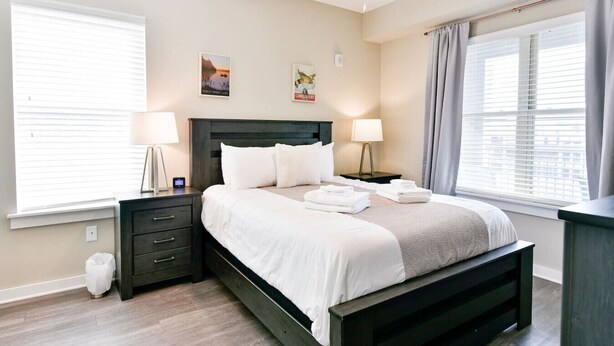 A bedroom with a bed, two bedside tables, a ceiling fan, and a window with curtains.