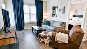 A modern living room with a sofa, a coffee table, a TV on a stand, and a window with curtains.
