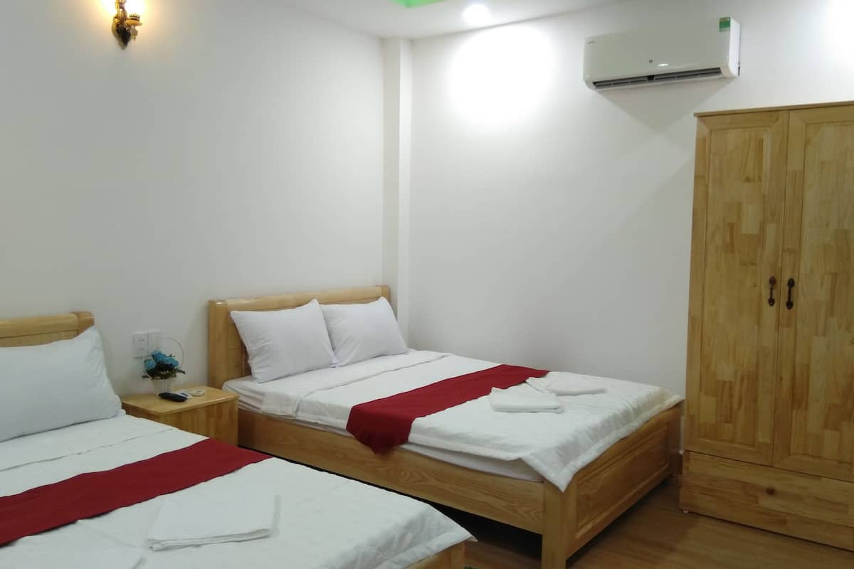 A hotel room with two single beds, a wooden wardrobe, and a wall-mounted air conditioner.