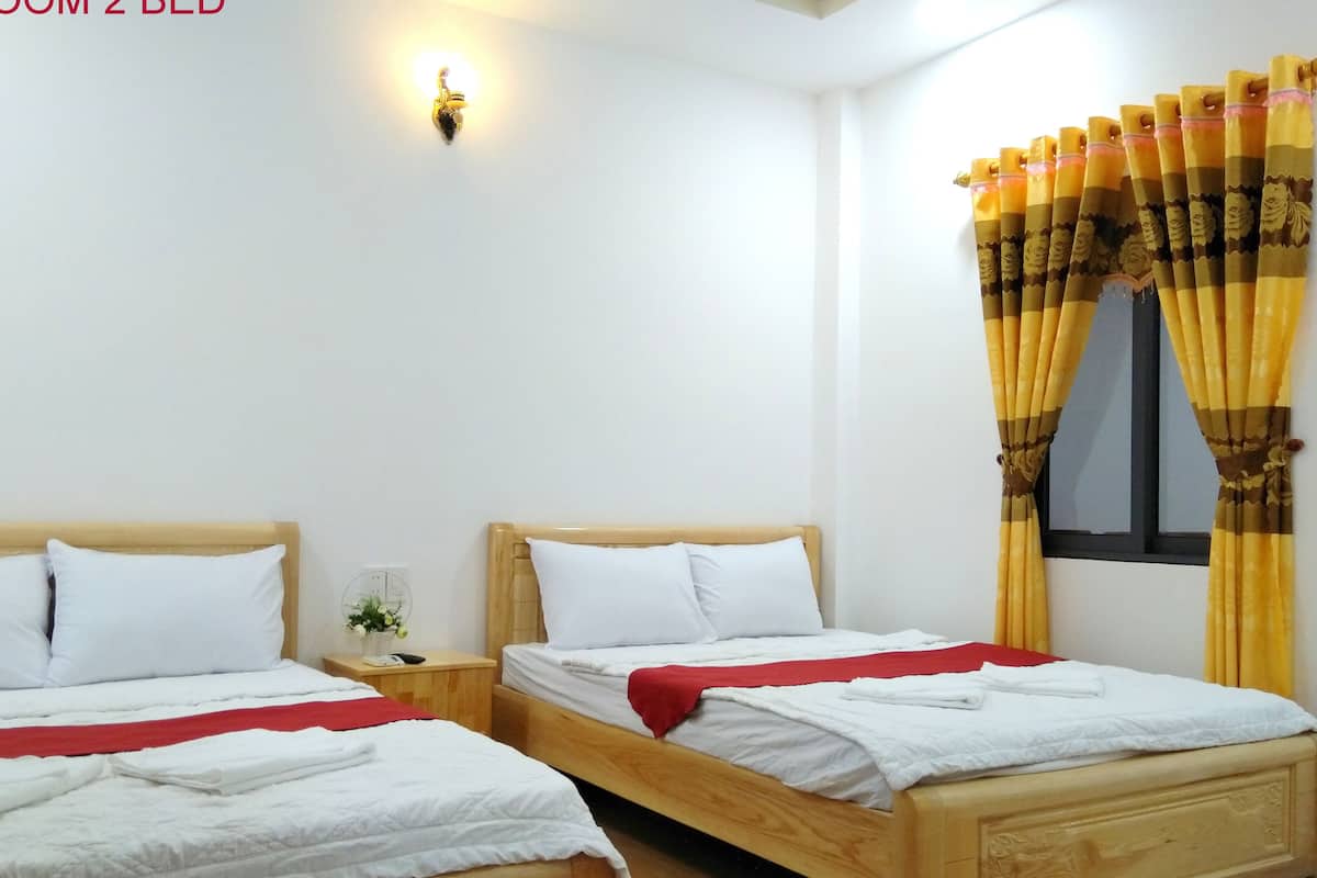 A hotel room with two wooden beds, white bedding, a red throw, a nightstand with a plant, and yellow curtains with floral patterns.
