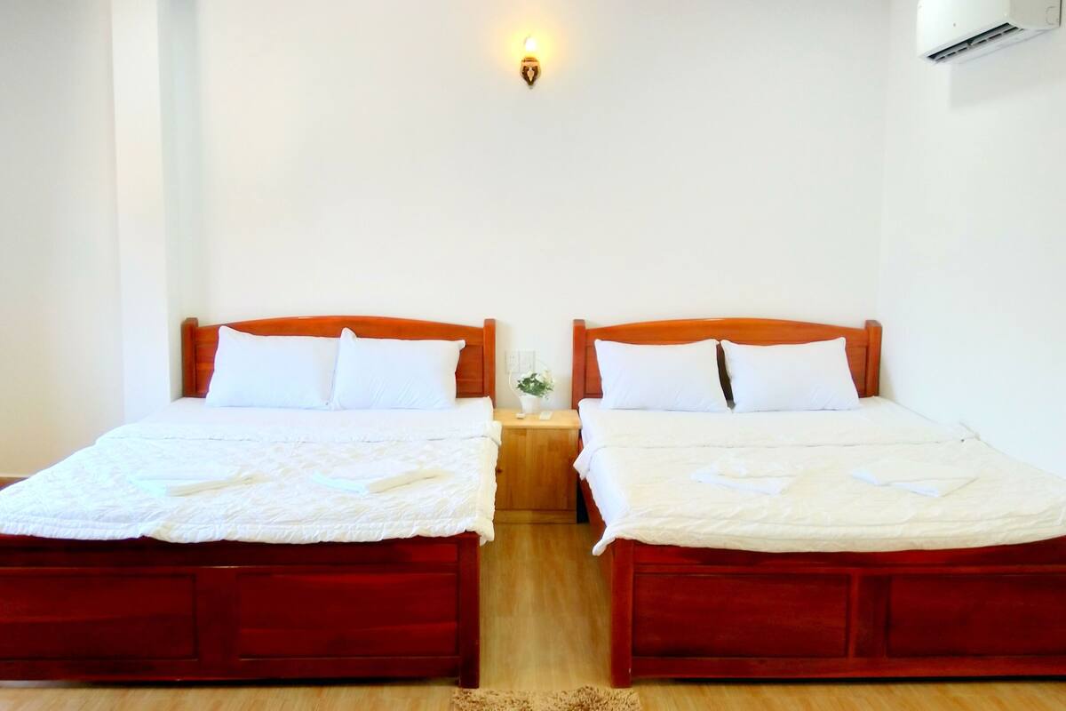 A hotel room with two beds, each with a wooden headboard, white bedding, and a small bedside table with a lamp.