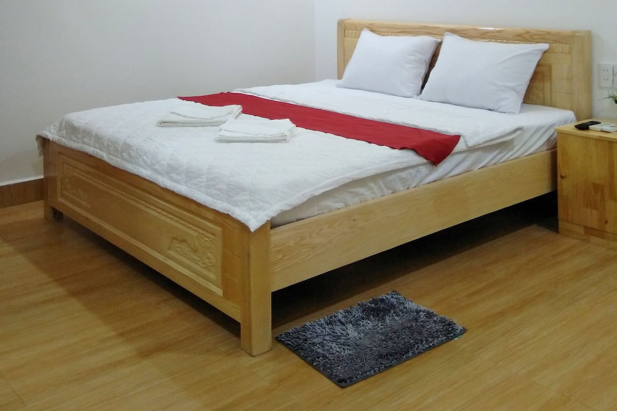 A neatly made bed with white linens and a red throw, a wooden headboard, and a small bedside table with a lamp.