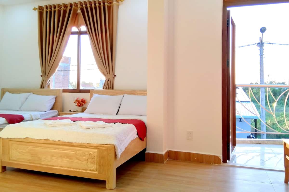 A bedroom with two beds, a window with curtains, and a view of greenery outside.