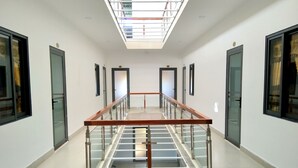 A modern hotel corridor with a glass railing, doors with numbers, and a skylight. - Hung Yen Hotel (Phu Quoc)