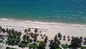 A beach with rows of umbrellas and palm trees, a sandy shore, and a clear blue sea. - Nina Apartments (Nha Trang)