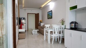 A compact living space with a kitchenette, a dining area with white chairs and a table, a sofa, and a painting on the wall. - Nina Apartments (Nha Trang)