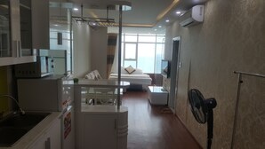 A hotel room with a bed, a TV, a fan, and a kitchenette. - Nina Apartments (Nha Trang)