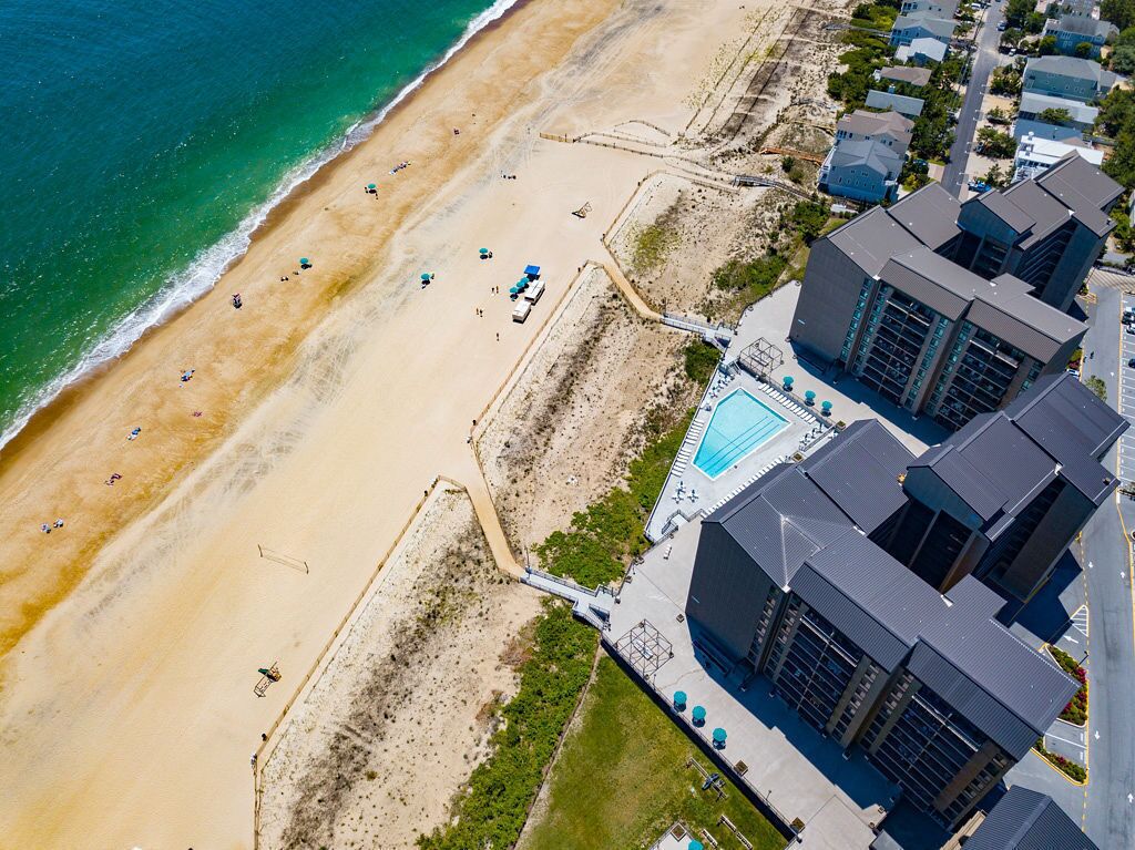 Vista aérea de um hotel à beira-mar, com praia, piscina e edifícios modernos.