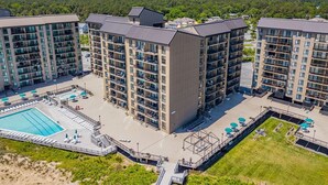 Un hotel moderno de gran altura con varios balcones, piscina y un patio ajardinado.