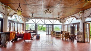 Une pièce spacieuse avec un plafond haut, de grandes fenêtres et un espace salon central comprenant une table et des chaises.