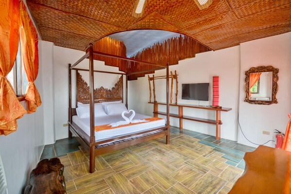 Un lit à baldaquin orné d’un motif en forme de cœur, une télévision et un miroir au mur.